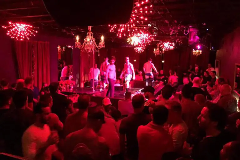 The inside of gay club Johnsons in Fort Lauderdale. It's lit in red, there are poles, and a crowd of people are surrounding the stage.